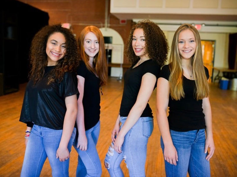 4 Girls are standing together wearing black t shirt and blue jeans